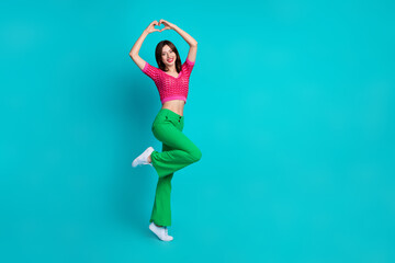 Full length photo of good mood lovely woman dressed knitwear top showing heart over head stand one leg isolated on blue color background