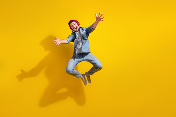 Fototapeta na wymiar Full length photo of carefree friendly man dressed jeans shirt jumping listening music open arms ready hug you isolated yellow color background