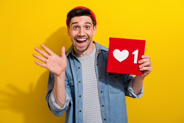Photo of friendly cheerful man dressed jeans shirt waving arm hi showing feedback card isolated yellow color background