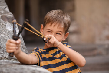 Cute little boy playing with slingshot outdoors