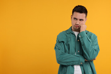 Fototapeta premium Resentful man with crossed arms on orange background, space for text