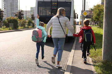 Being late for school. Senior woman and her grandchildren with backpacks running towards bus...