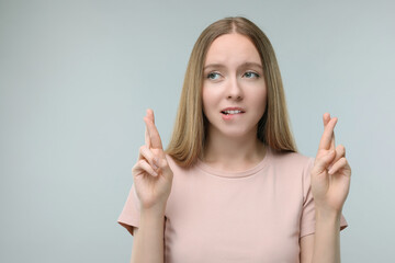 Woman crossing her fingers on grey background, space for text