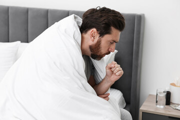 Fototapeta premium Sick man coughing on bed at home. Cold symptoms