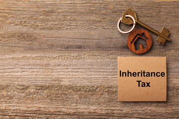 Inheritance Tax. Card and key with key chain in shape of house on wooden table, flat lay. Space for...