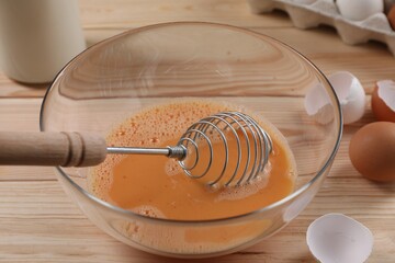 Making dough. Beaten eggs in bowl and shells on wooden table, closeup