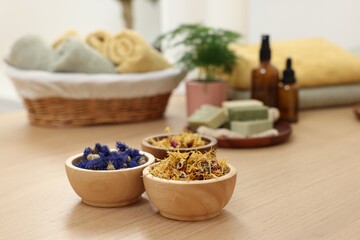 Bowls of dry flowers on light wooden table, space for text. Spa therapy