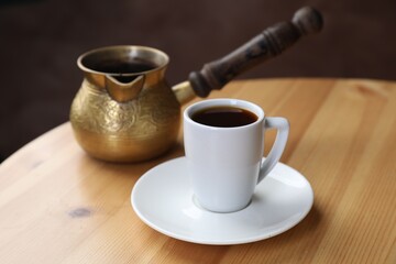 Turkish coffee. Freshly brewed beverage in cup and cezve on wooden table