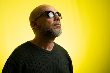 White man, bald, wearing sunglasses, serious and thoughtful.