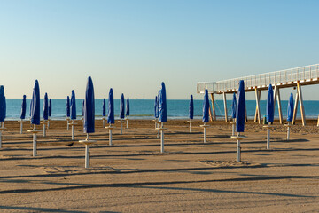 Closed beach umbrella waiting for beach-goers to arrive in early morning light with long shadows