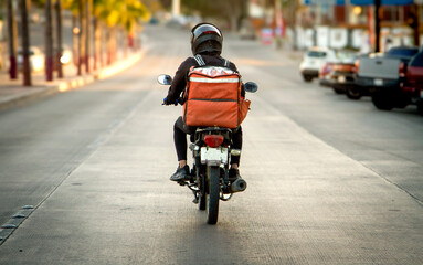 Food service worker on a motorcycle on a highway photographed rom behind