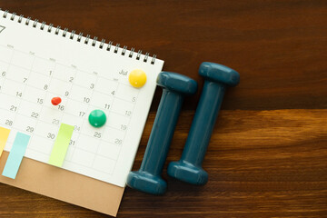 close up of calendar and dumbbell on the wooden table background, planning for sport or exercise concept