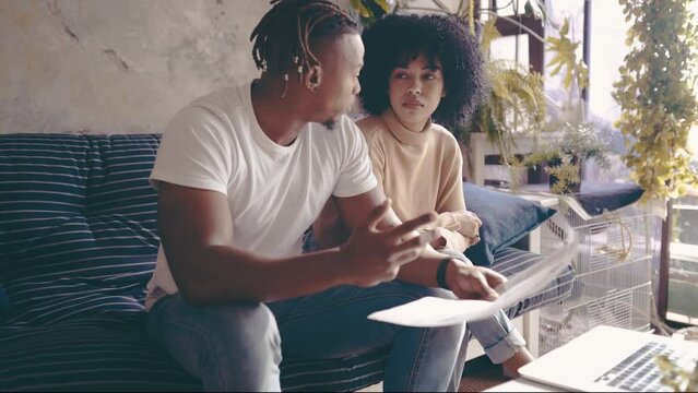 Black couple, laptop and paperwork in financial debt, budget planning or expenses on sofa at home. African man and woman with documents on computer for finance, bills or invoice together at house