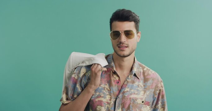 Happy man, sunglasses and fashion with cool shirt posing in style against a green studio background. Portrait of handsome, attractive or young male person or model in stylish clothing on mockup space