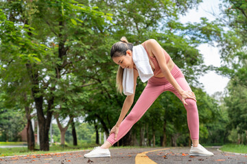 Young attractive Asian woman stretching her arms and legs before her morning exercise run at running track of a local park