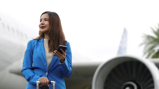 Businesswoman at the airport carries a suitcase, prepares to board the plane and depart. Young Asian business woman at the airport is using a smartphone to contact someone.