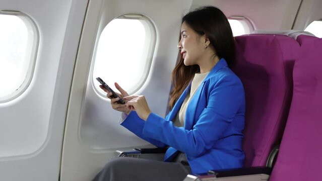 Attractive Asian businesswoman traveling on airplane playing with mobile phone while sitting in cabin.