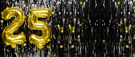 Gold foil balloon number number 25 on a background of black tinsel decoration. Birthday greeting...