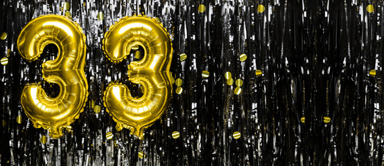 Gold foil balloon number number 33 on a background of black tinsel decoration. Birthday greeting card, inscription thirty three. Anniversary event. Banner.