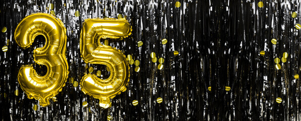 Gold foil balloon number number 35 on a background of black tinsel decoration. Birthday greeting...