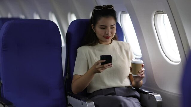 Happy young Asian woman traveling alone playing with mobile phone on airplane, she is texting with friends.