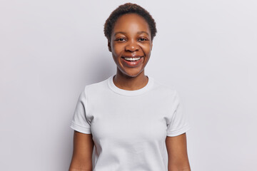 People positive emotions concept. Indoor shot of young happy smiling broadly African american female wearing casual clothes standing isolated on centre on white background keeping hands down