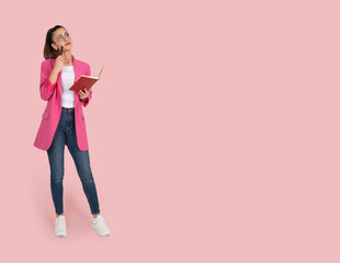 Thoughtful concentrated woman, full body portrait of charming thoughtful concentrated woman. Holding pen and notepad, thinking looking copy space. Isolated pastel pink background. Advertisement idea.