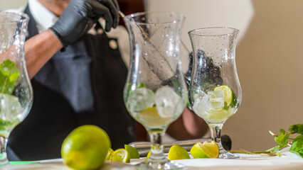 Bartender making cocktails in glasses on the bar counter. Lemon and mint flavor.