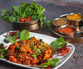 Spicy Indian chicken curry with tomato, coriander, masala, and leaves on plates.