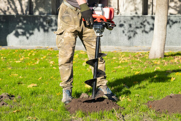 Gardener using tools hand-held soil hole drilling machine or portable manual earth auger.