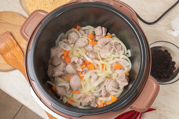 Frying meat with onions and carrots in a multicooker pan. Modern, bright multi cooker with products. Cooking pilaf with meat in multicooker. Multi cooker with vegetables and meat.
