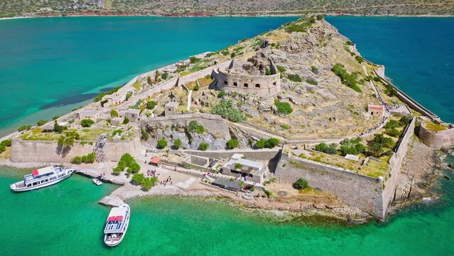 Scenic Aerial view of antique Fortress Island in Crete, Greece with tourists visiting. Spinalonga barren arid rocky islet in Elounda. Venetians built bastion-type seaward fortresses in Mediterranean