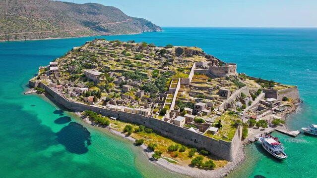 Scenic Aerial view of antique Fortress Island in Crete, Greece with tourists visiting. Spinalonga barren arid rocky islet in Elounda. Venetians built bastion-type seaward fortresses in Mediterranean