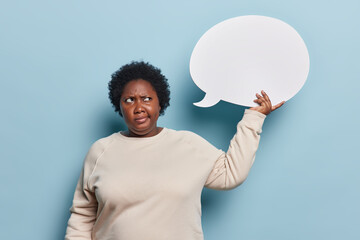 Photo of displeased dark skinned overweight woman wears casual jumper holds blank speech bubble for...