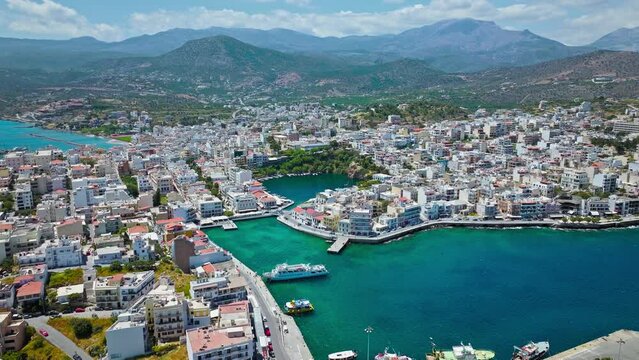 Aerial panoramic view of Agios Nikolaos City on Crete Island in Greece in 4K. Sunny summer City day on Mediterranean Island with turquoise water. Paralia Kitroplatia, Ammos, Yachting Sailing Cruises