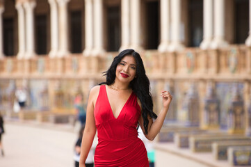 Young and beautiful brunette and latin woman, dressed in short red dress and red shoes visits the famous square of seville, spain, international monument and where different movies have been filmed.