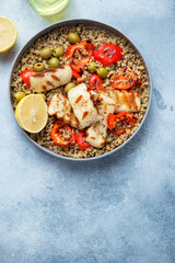 Plate of quinoa with grilled halloumi, red bell pepper and green olives, flat lay on a light-blue stone background, vertical shot, copy space