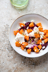 Plate with roasted sweet potato, radicchio and feta cheese, vertical shot on a beige granite background, selective focus