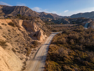 Dirt road in arid desert landscape with distant cliffs and morning sunlight, Elche, Alicante province, Spain - Stock photo