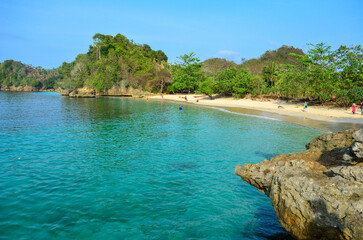 A tranquil coastal scene featuring a sandy beach, clear turquoise water, and lush green islands.