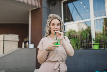 A young blonde woman plus size model sits with a cocktail on the summer area of a city cafe.