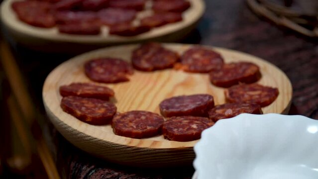 Closeup, one person placing some chorizo and fuet slices on a wooden plate