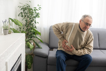 Senior man having stomach pain sitting at home.