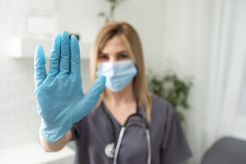 a girl in medical gloves and a protective mask shows a stop sign with her palm. safe distance. Covid-19 coronavirus epidemic. protective measures against infection