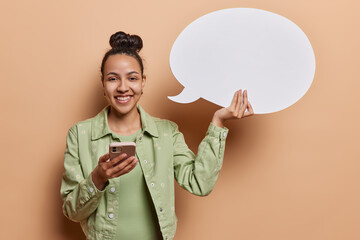 People positive emotions concept. Studio shot of young happy smiling European woman standing isolated on left on beige background wearing casual clothes holding white speech bubble with space