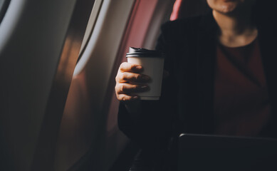 Blonde female tourist checking incoming notification on smartphone sitting on seat of airplane with netbook.Young businesswoman share media from telephone on laptop computer during plane flight