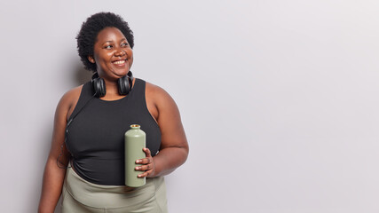 Sporty and healthy lifestyle. Studio waist up of young plump happy smiling African american woman standing on left isolated on white background wearing tracksuit after exercises to lose weight - obrazy, fototapety, plakaty