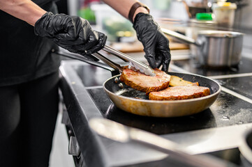 Professional chef cooking beef steak in frying pan on stove in restaurant kitchen