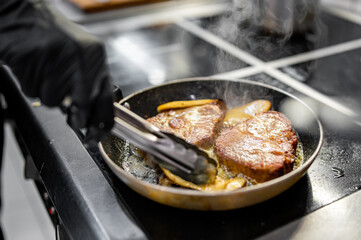Professional chef cooking beef steak in frying pan on stove in restaurant kitchen