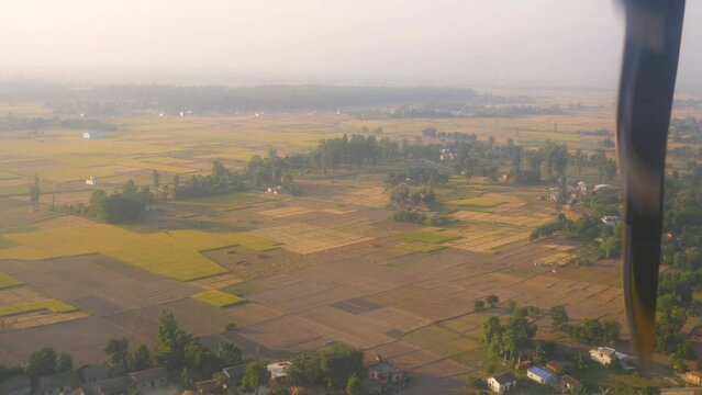 Timelapse from inside of an airplane landing in an airport in a foggy environment with a view of plain land with forest, crops emitting beautiful green and yellow texture